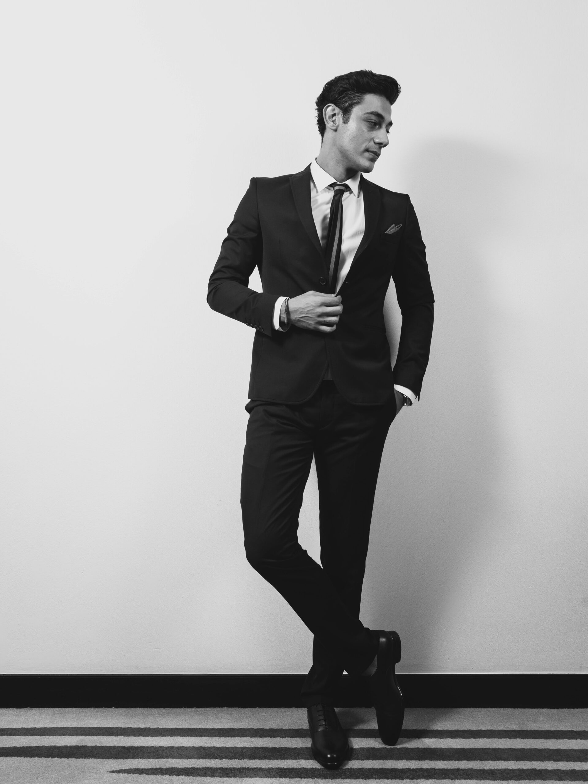 Black and white portrait of a sophisticated man in formal attire striking a confident pose.