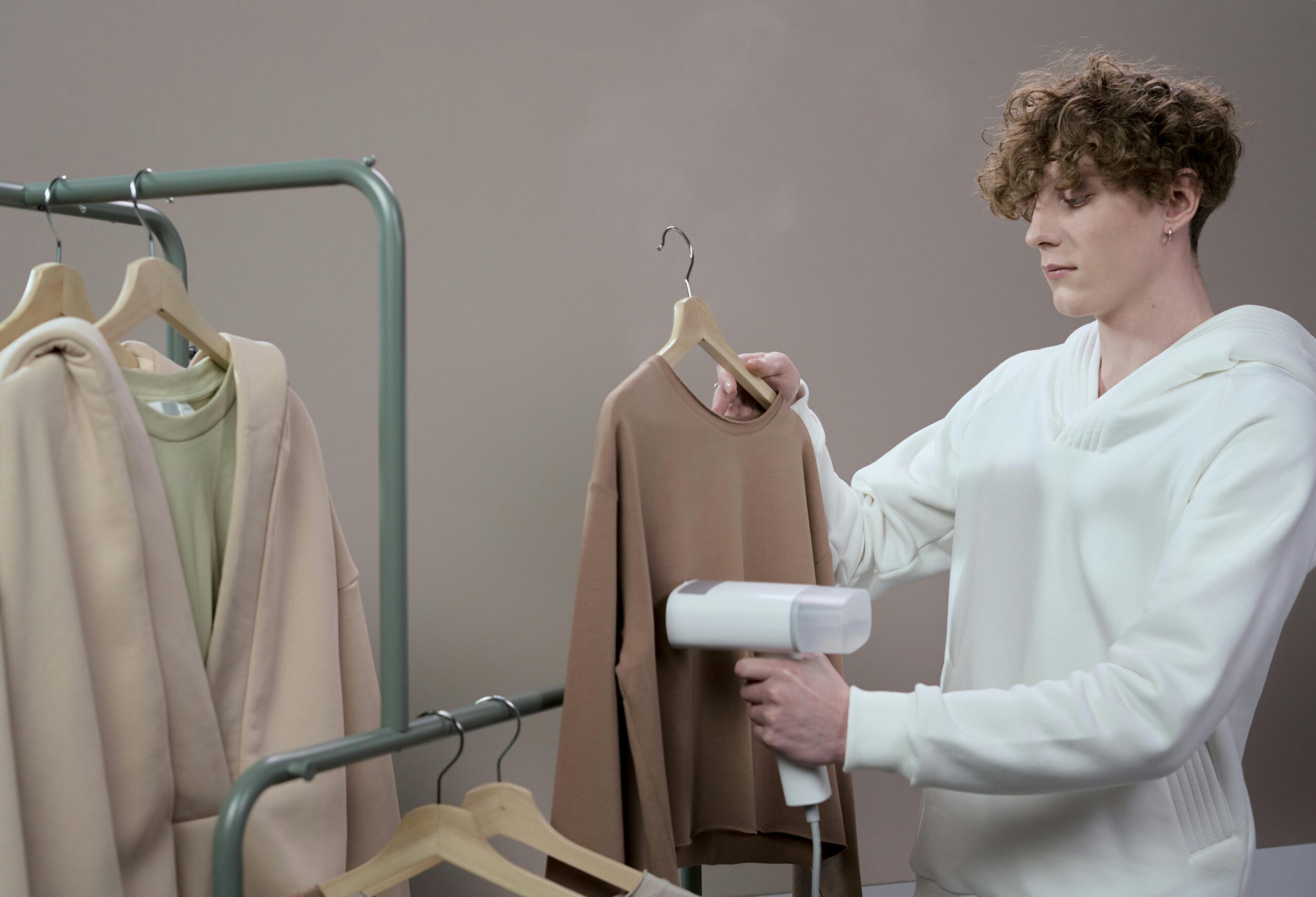Young man steaming a sweatshirt in a fashion studio setting with casual clothes.